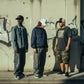 Três homens com bonés astredik UNIFORM 00 de aba curva em ambiente urbano com graffiti ao fundo