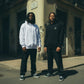 Dois modelos usam hoodies astredik UNIFORM 00 em branco e preto com logótipo bordado, em ambiente urbano.